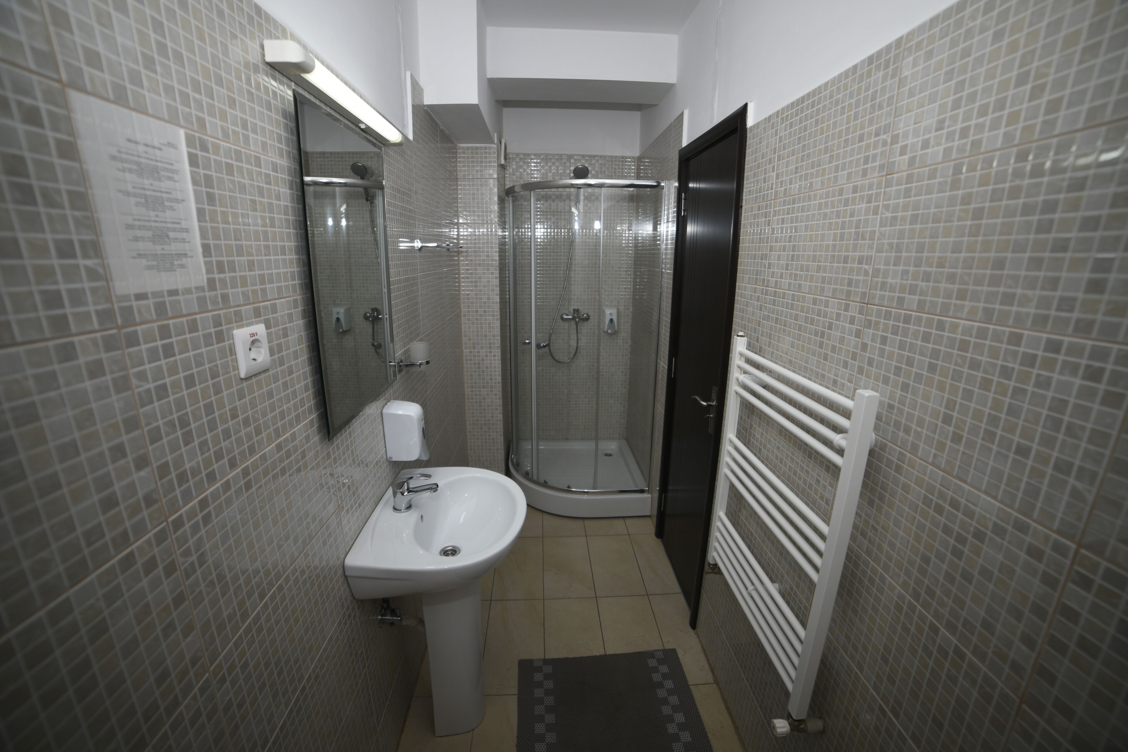 Un baño con cabina de ducha de vidrio, un lavamanos y un perchero para toallas.