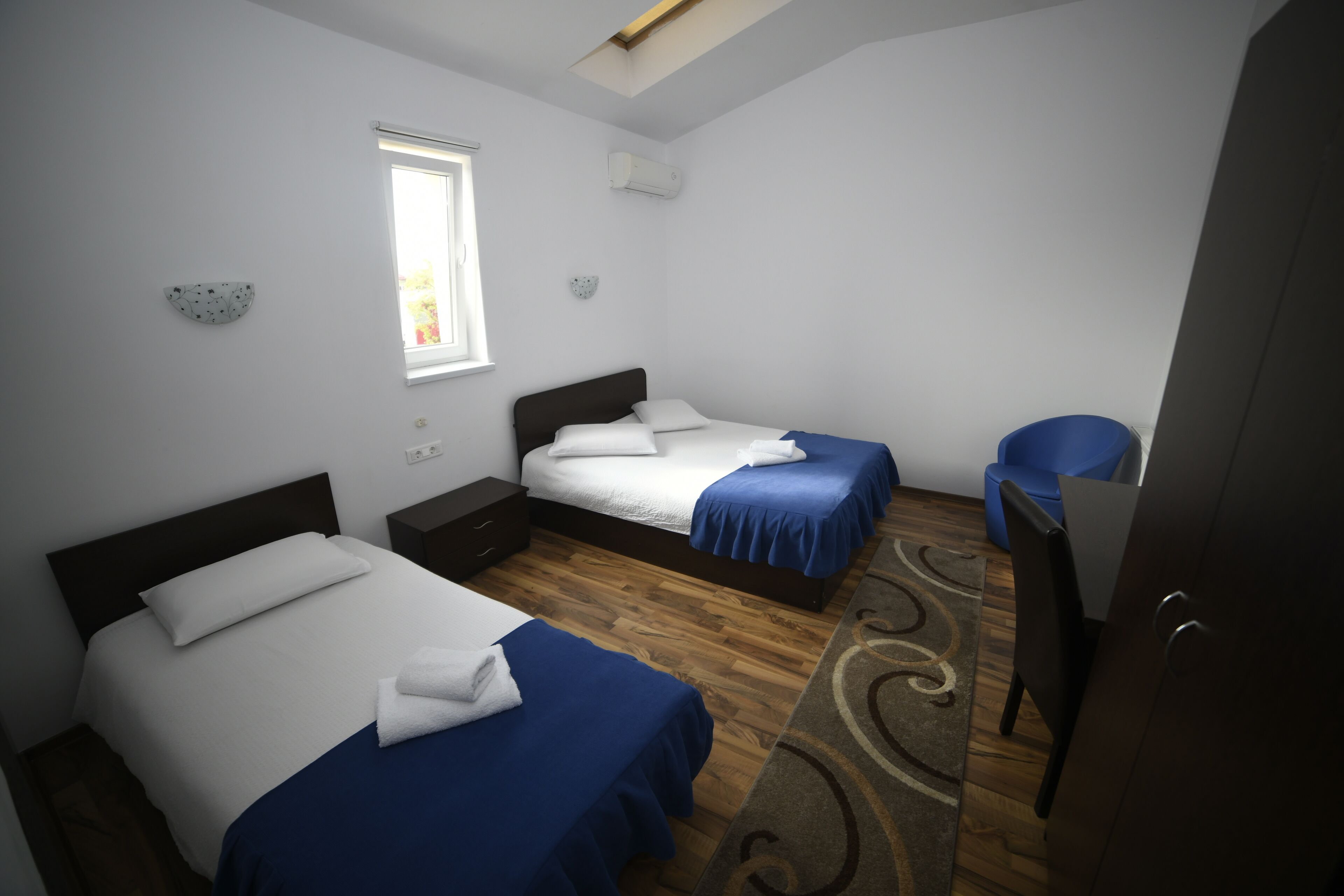 A bedroom with two beds, a window, a desk, and a chair.