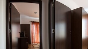 Un couloir avec un plancher en bois, un téléviseur posé sur un meuble, et une pièce avec un lit et des rideaux en arrière-plan.