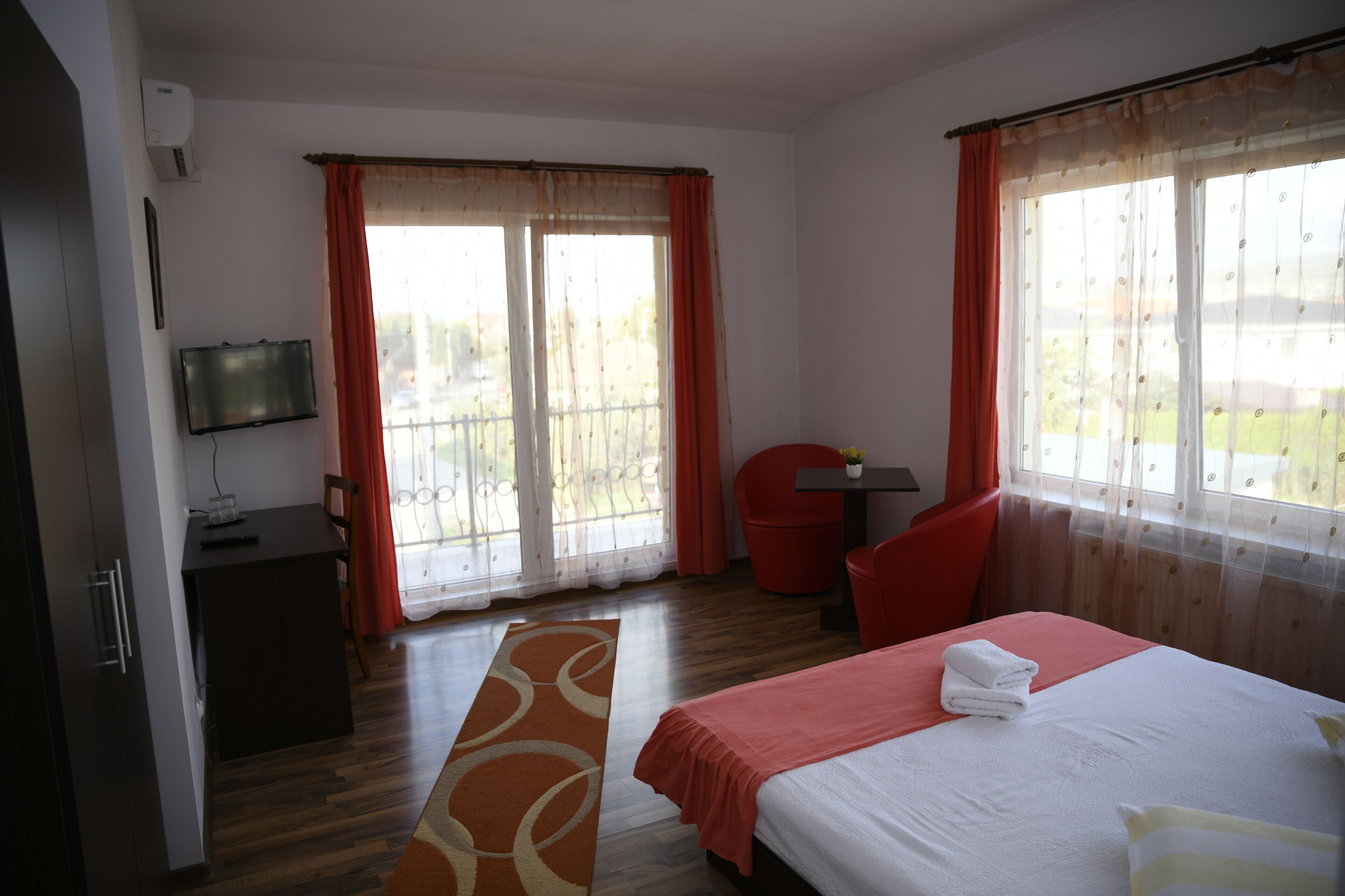 A hotel room with a bed, a desk, a chair, a TV, and a window with curtains.