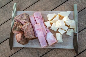 A wooden cutting board with sliced meats and cheese on a rustic table. - The Millers House Adamas Sea View (Milos)