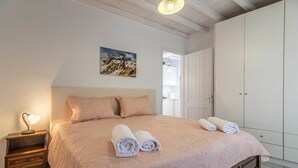 A bedroom with a large bed, two pillows, a bedside table with a lamp, and a painting on the wall. - The Millers House Adamas Sea View (Milos)
