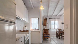 A kitchen with white cabinets, a stove, and a sink. There is a dining area with a table and chairs. - The Millers House Adamas Sea View (Milos)