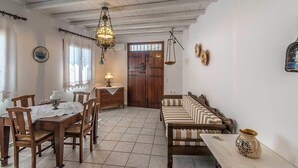 A dining area with a wooden table and chairs, a hanging chandelier, and a sofa with striped cushions. - The Millers House Adamas Sea View (Milos)