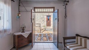 A room with a wooden bench, a small table with a lamp, and a door leading to an outdoor area with a stone wall and wooden steps. - The Millers House Adamas Sea View (Milos)