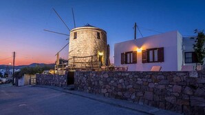 Un edificio con pareti in pietra e una torre rotonda, e un altro edificio bianco con persiane di legno.