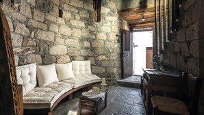 Una stanza con pareti in pietra, una panca imbottita, un tavolino e una sedia.