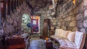 Una stanza con pareti in pietra, un tavolo di legno, una panca imbottita e una candela su un tavolino.