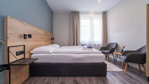 Una habitación de hotel moderna con cabecera de madera, una cama grande, un escritorio, dos sillas y una mesita.