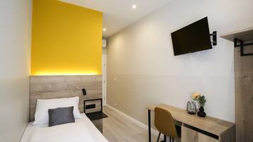 A modern hotel room with a bed, a desk, and a TV mounted on the wall.