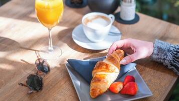 A table with a croissant, strawberries, a glass of orange juice, a cup of coffee, and a pair of sunglasses.
