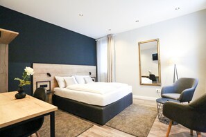 A modern bedroom with a large bed, a wooden desk, a chair, a mirror, and a lamp.