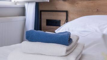 Un lit bien fait, avec des serviettes blanches et bleues, une tête de lit en bois et une fenêtre donnant sur des arbres.