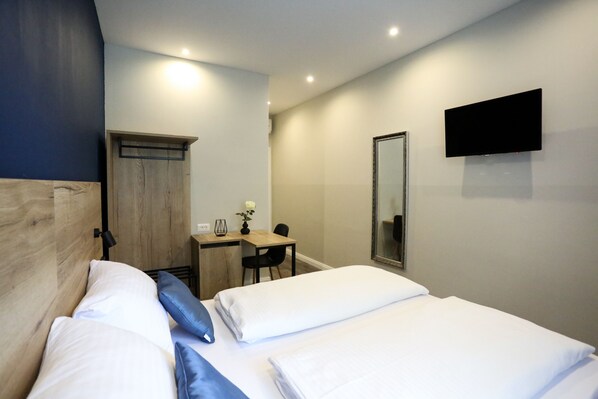 Habitación de hotel con cama, escritorio, silla, televisor y espejo.