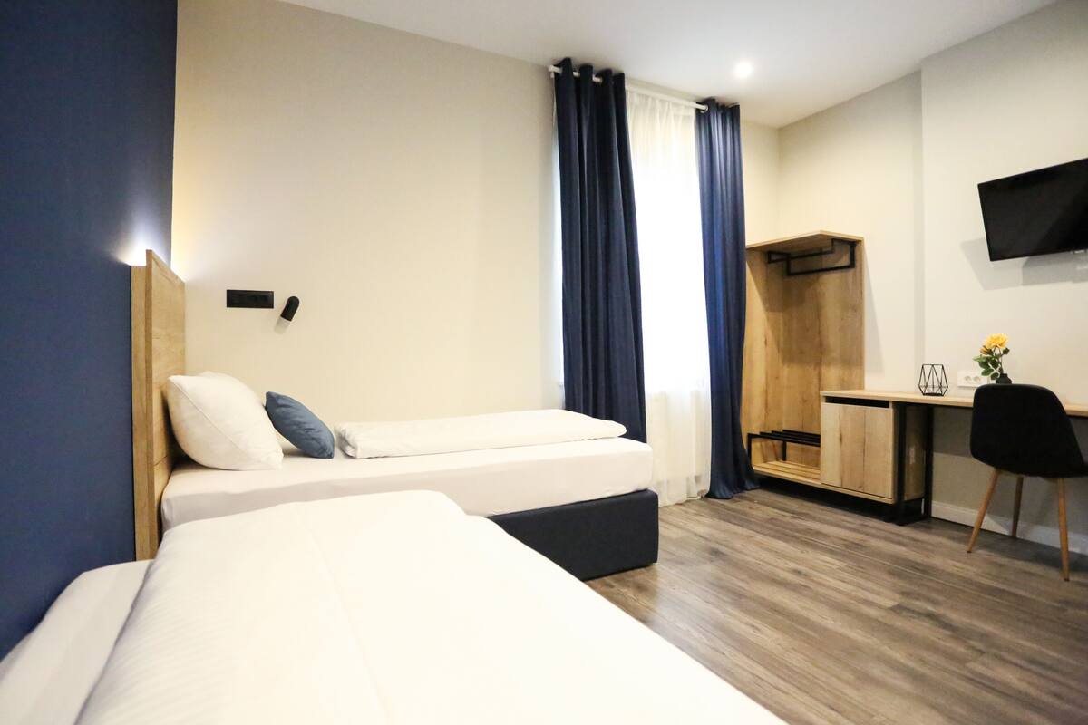 A hotel room with two beds, a desk, a chair, a TV, and a wardrobe.