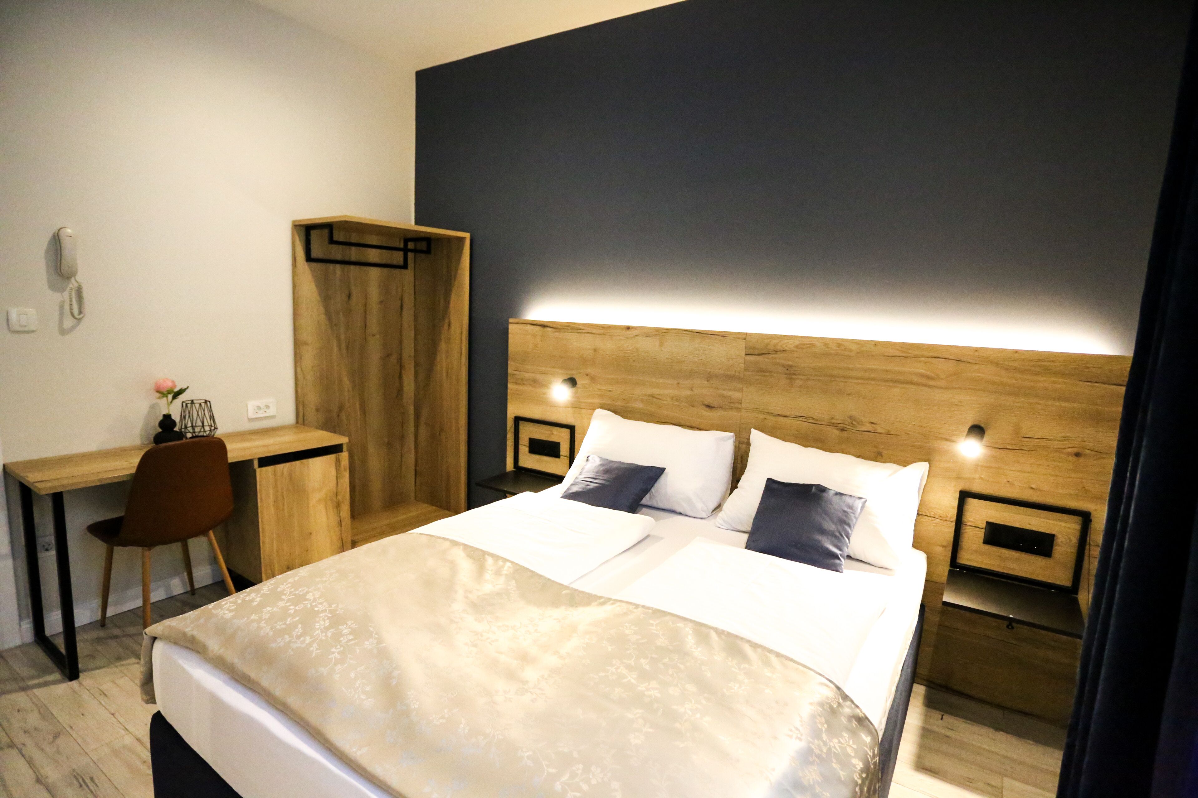 Hotellihuoneessa on suuri sänky, työpöytä ja tuoli. Sängyn päädyssä on puinen koristepaneeli, sängyn vieressä on yöpöydät ja seinällä puhelin.