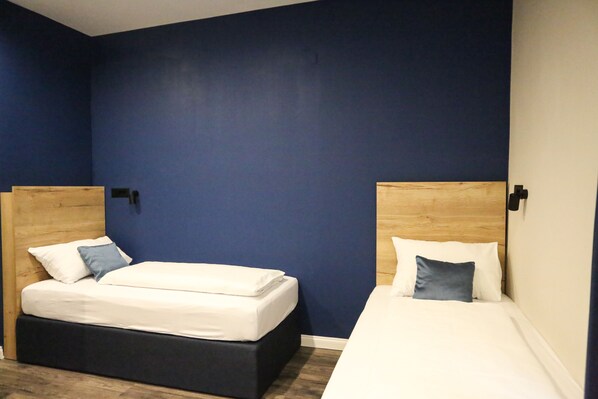 A room with two beds, each with a wooden headboard, white bedding, and a blue pillow.