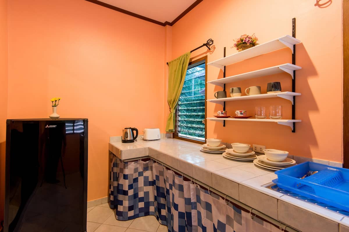 Una cocina compacta con refrigerador, una ventana con cortinas, un estante con utensilios de cocina y un escurreplatos azul.