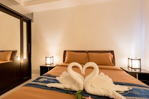 A hotel room with a bed, two nightstands, a mirror, and a decorative swan towel arrangement.