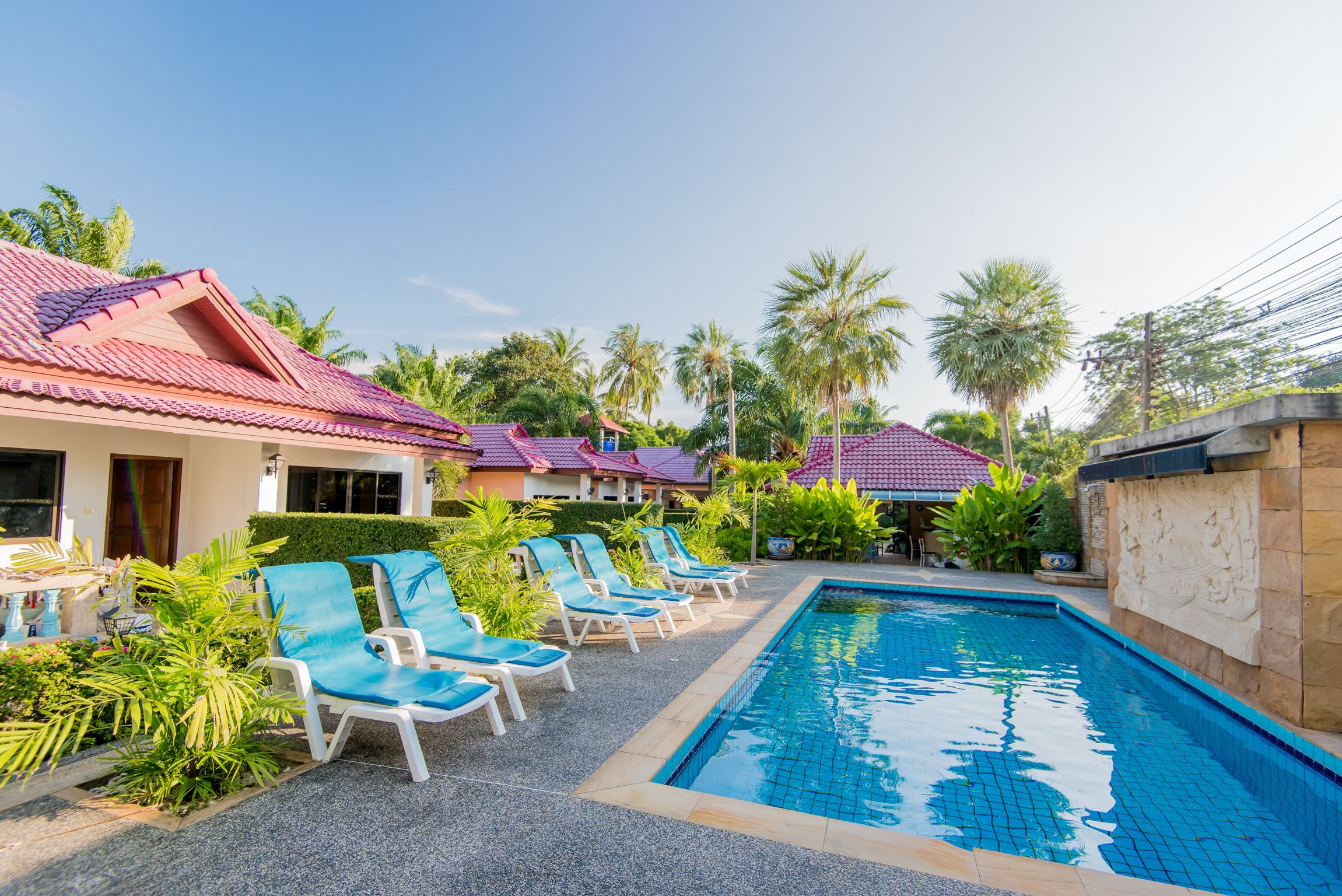 Ein Swimmingpool mit Liegestühlen, Palmen und Gebäuden mit roten Dächern.
