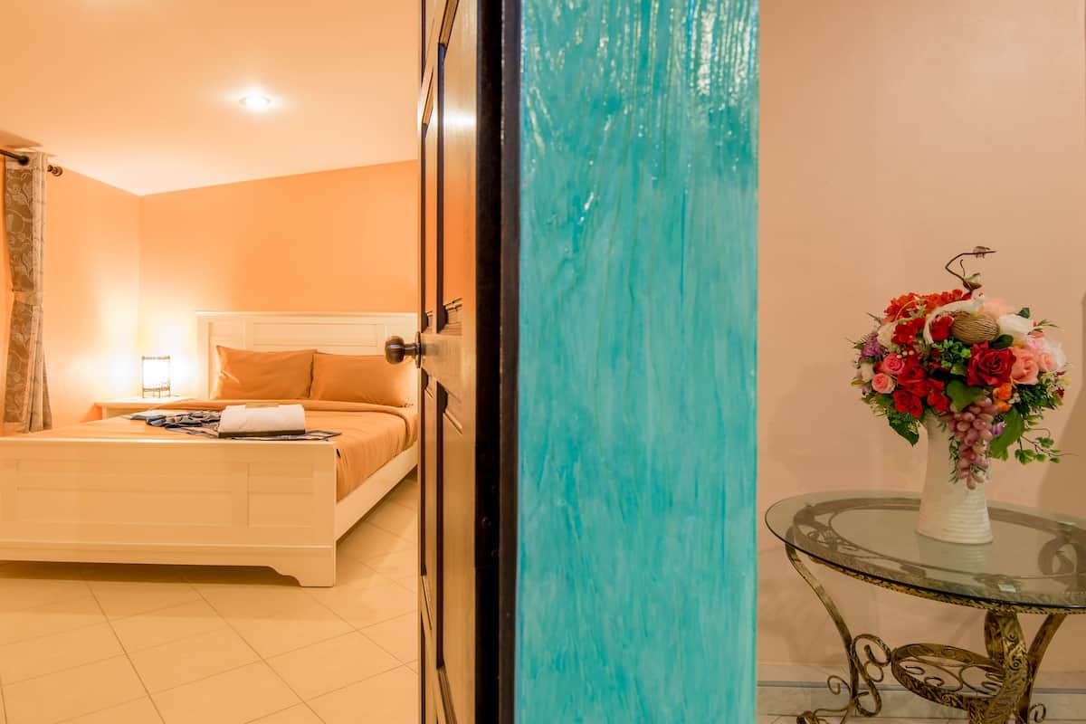 Una habitación de hotel con una cama, una mesita de noche, una lámpara y un jarrón con flores sobre una mesa.