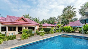 A pool area with a tiled pool, surrounded by palm trees and a building with a red roof.
