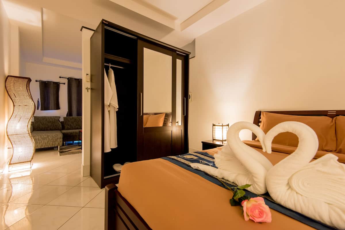 Una habitación de hotel con cama, una zona de estar con sofá y un baño con espejo y perchero para toallas.