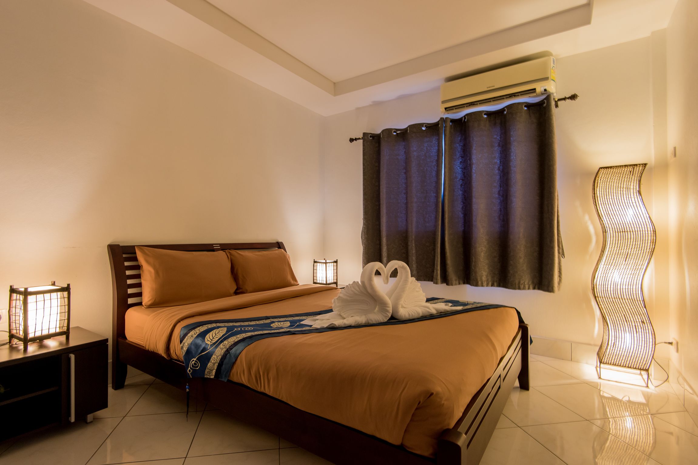 A hotel room with a large bed, a nightstand, a wall-mounted air conditioner, and a unique light fixture.