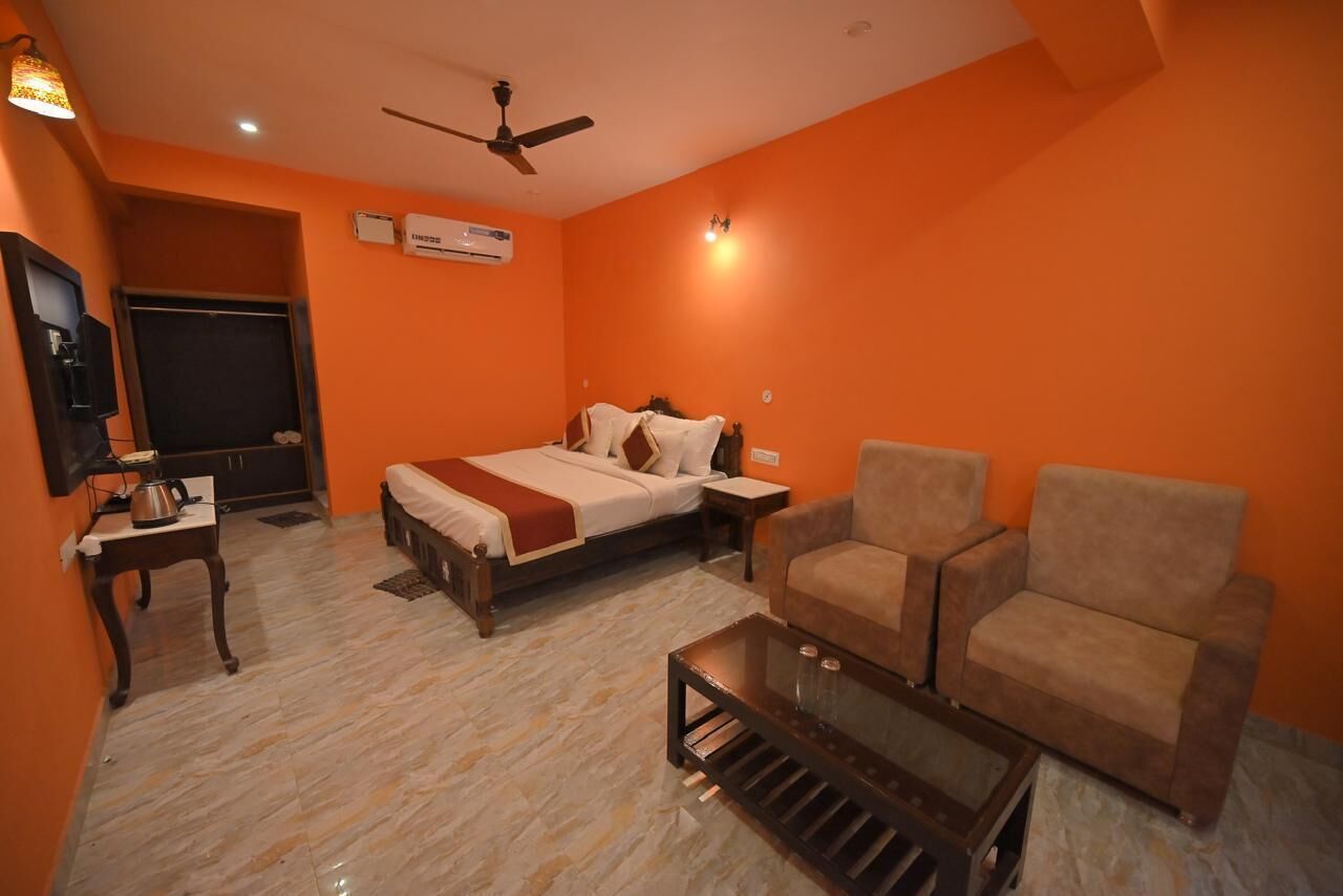 A hotel room with a bed, two armchairs, a coffee table, a television, and an air conditioning unit.