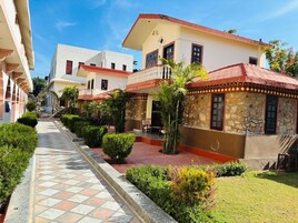 Un cortile con un vialetto piastrellato, edifici in pietra con tetti rossi e vegetazione curata.