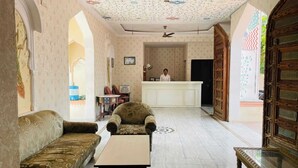 A hotel lobby with a reception desk, a sofa, a chair, and a small table. - Sajjan Bagh Resort (Pushkar)