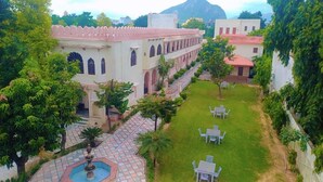 A courtyard with a fountain, seating area, and a building with arched windows and a tiled roof. - Sajjan Bagh Resort (Pushkar)