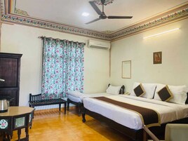 Camera d'albergo con un letto, una scrivania, una sedia, una ventola a soffitto e una finestra con tende a fiori.