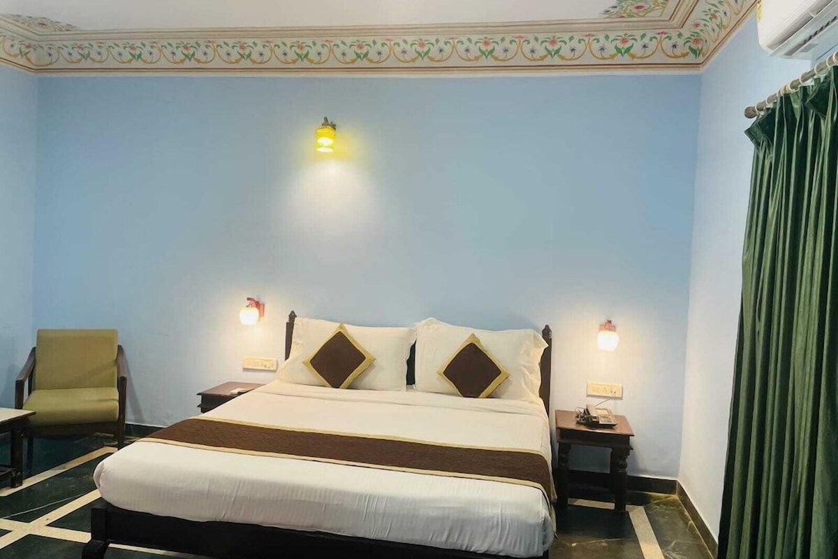 A hotel room with a bed, two bedside tables, a chair, and a green curtain.