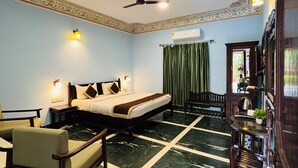 A hotel room with a bed, a desk, a chair, a ceiling fan, and a marble floor. - Sajjan Bagh Resort (Pushkar)