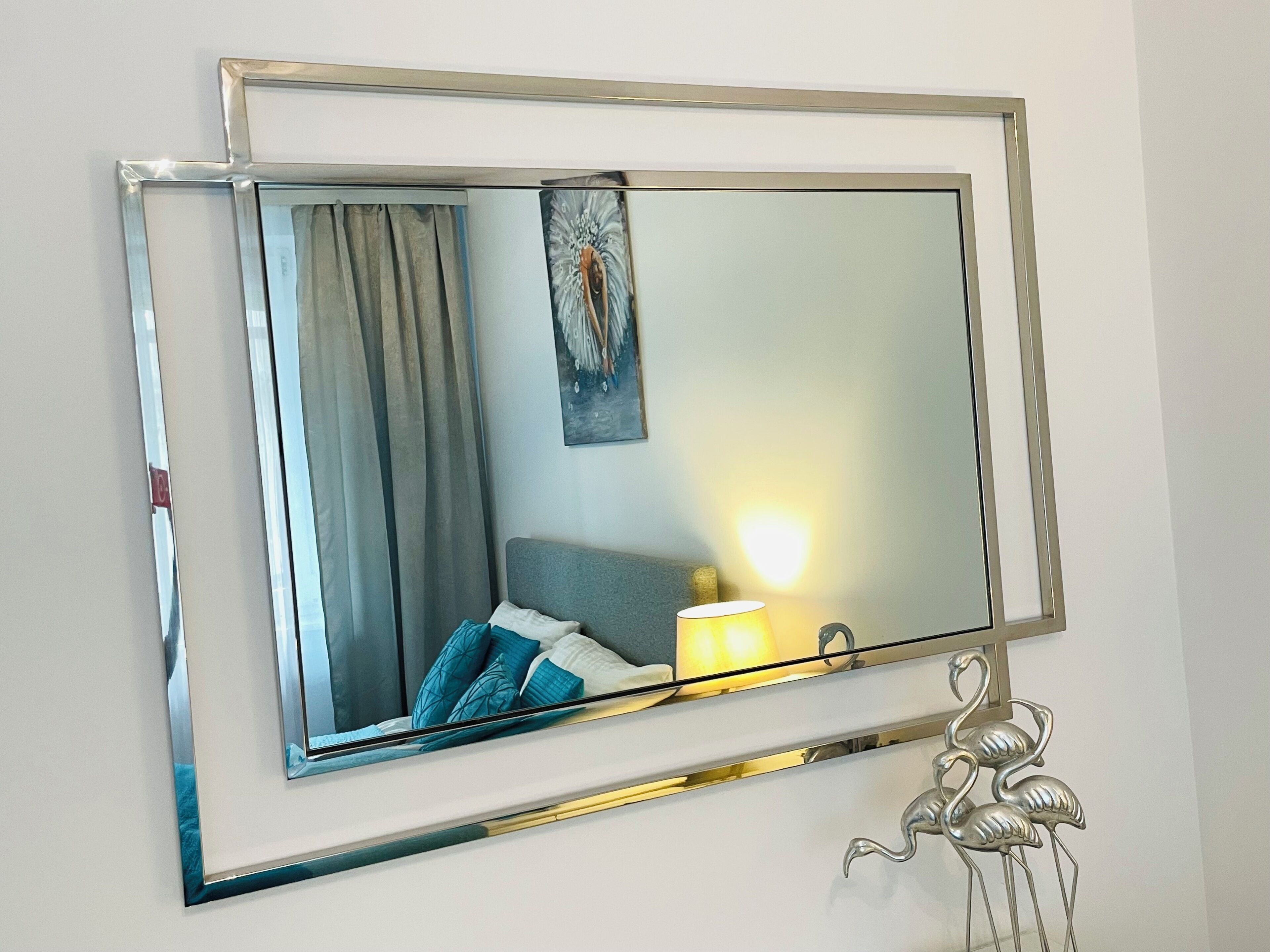 A mirror with a metallic frame, a lamp, and a wall-mounted sculpture.