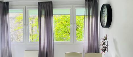A room with a dining table, chairs, a clock, and a window with curtains.