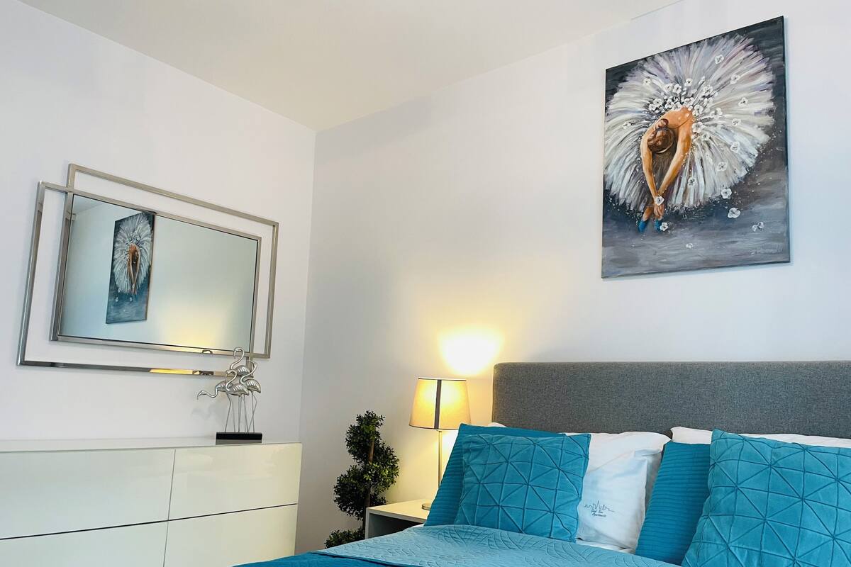 Una camera da letto con un letto, un comodino, una lampada, uno specchio e un quadro appeso al muro.