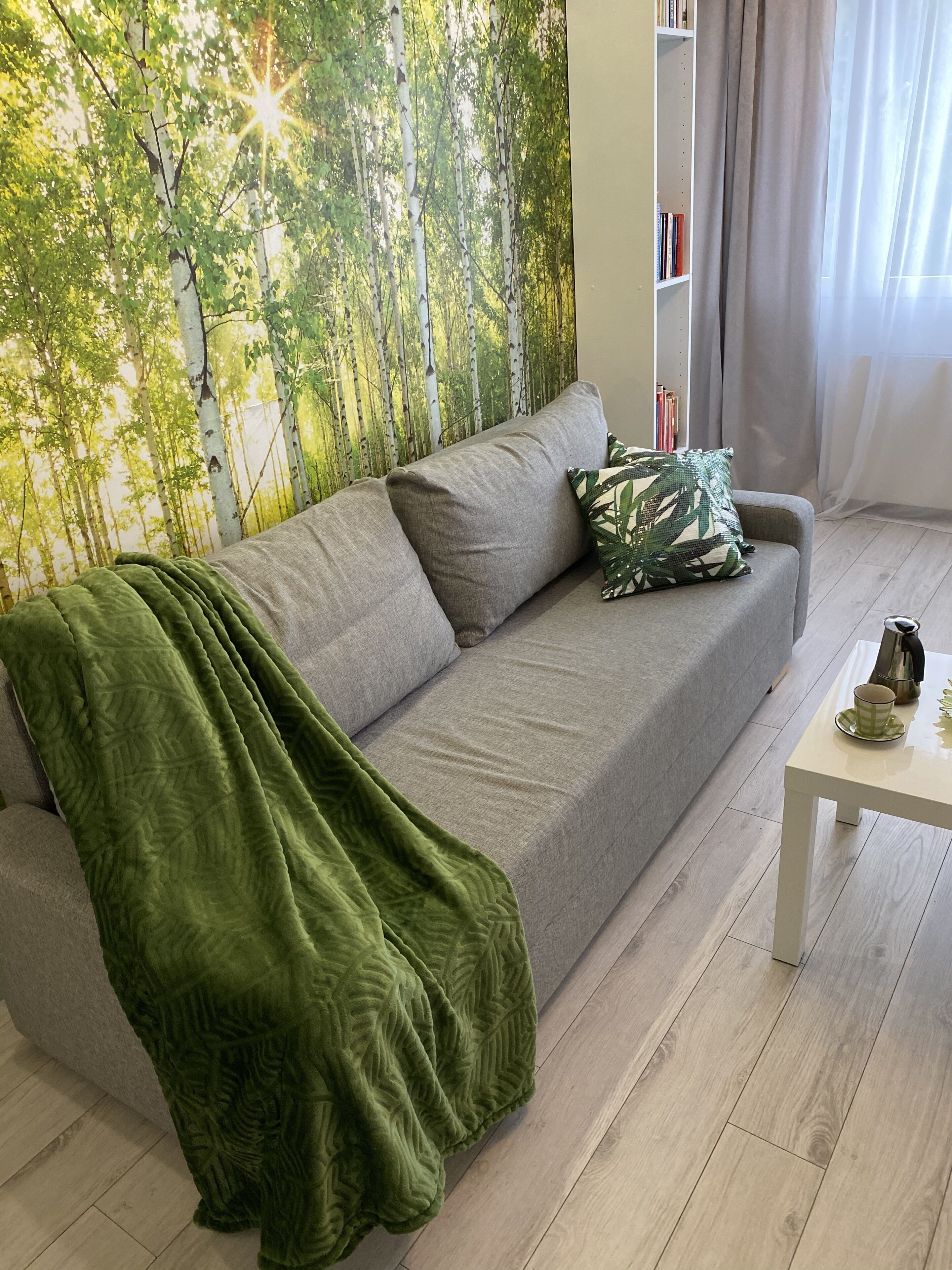 A modern living room with a grey sofa, a green throw blanket, and a white coffee table with a cup and saucer.