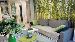 A modern living room with a grey sofa, green cushions, a glass coffee table with green placemats, a green vase with flowers, and a wall with a vertical garden. - Good Time Apartments (Warsaw)