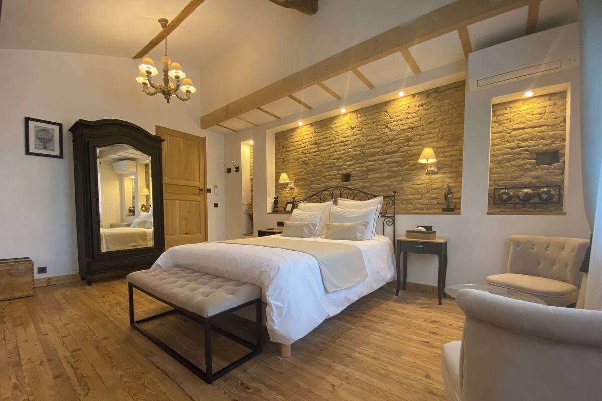 Ein Schlafzimmer mit einem großen Bett, Holzboden, Steinwand und einem Sessel.