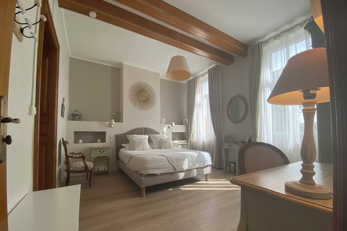 Ein Schlafzimmer mit einem Bett, Nachttischen, einem Sessel, einem Schreibtisch und einer Lampe.