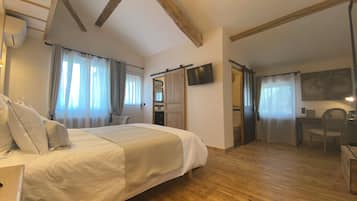 Ett hotellrum med en stor säng, trägolv, en platt-TV, ett skrivbord med en stol och ett badrum som syns genom en öppen dörr.