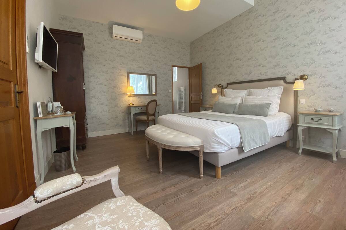 Ein Schlafzimmer mit einem Bett, Nachttischen, einem Schreibtisch, einem Stuhl, einem Fernseher und einer Klimaanlage.