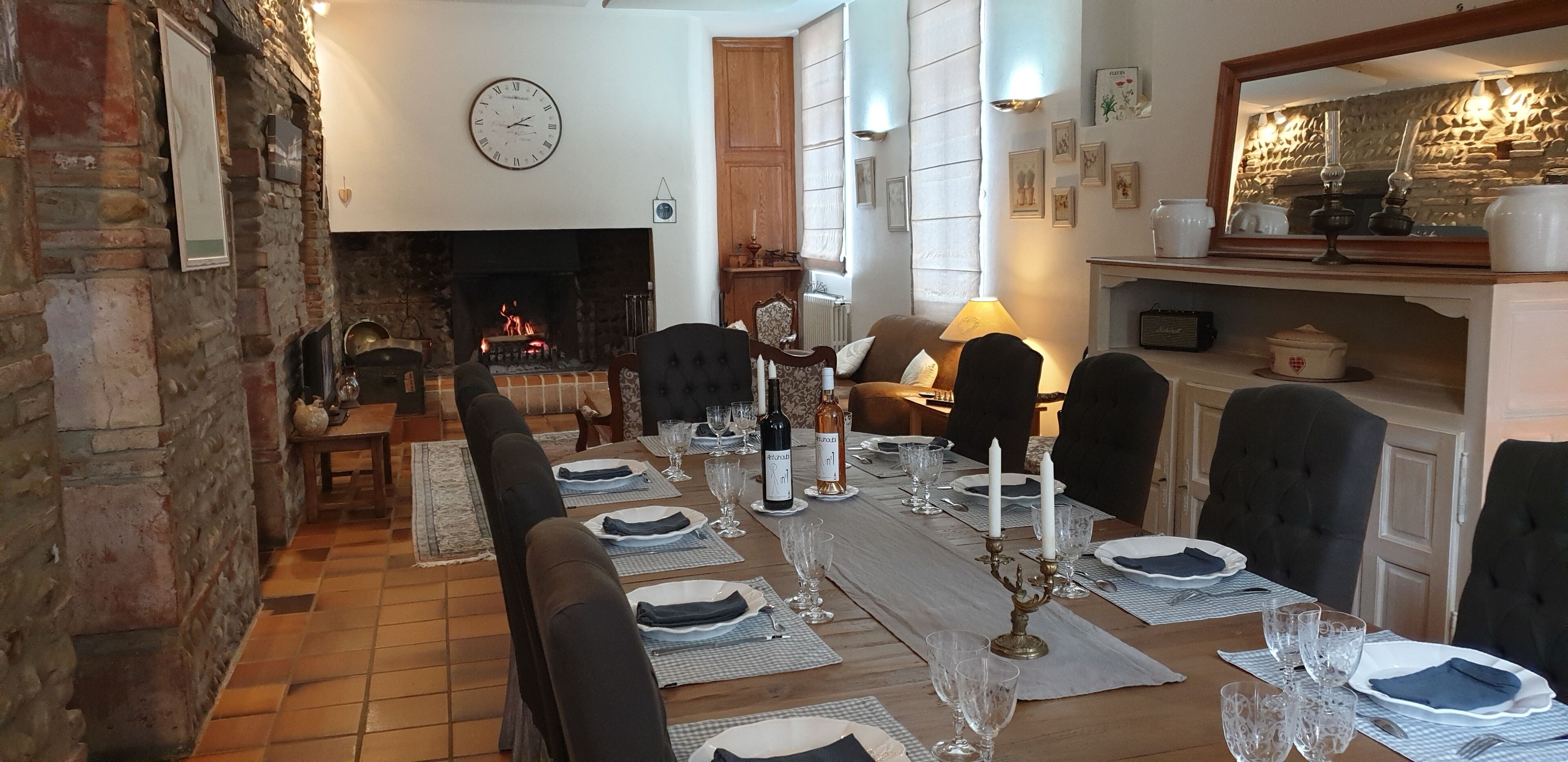 A dining room with a long table set for a meal, a fireplace, and a clock on the wall.