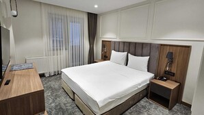 A modern hotel room with a large bed, a wooden desk, a nightstand, and a window with sheer curtains. - Gemlik Pasa Hotel (Gemlik)