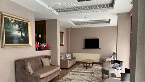 A modern living room with a sofa, armchairs, a coffee table, and a TV. - Gemlik Pasa Hotel (Gemlik)