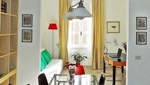 A living room with a white sofa, a glass coffee table, a red lamp, and a laptop on a wooden desk. - Vittorino Guest House (Rome)