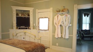 A bedroom with a bed, a television, a dresser, and two robes hanging on the wall. - The Carleton House (Bonham)