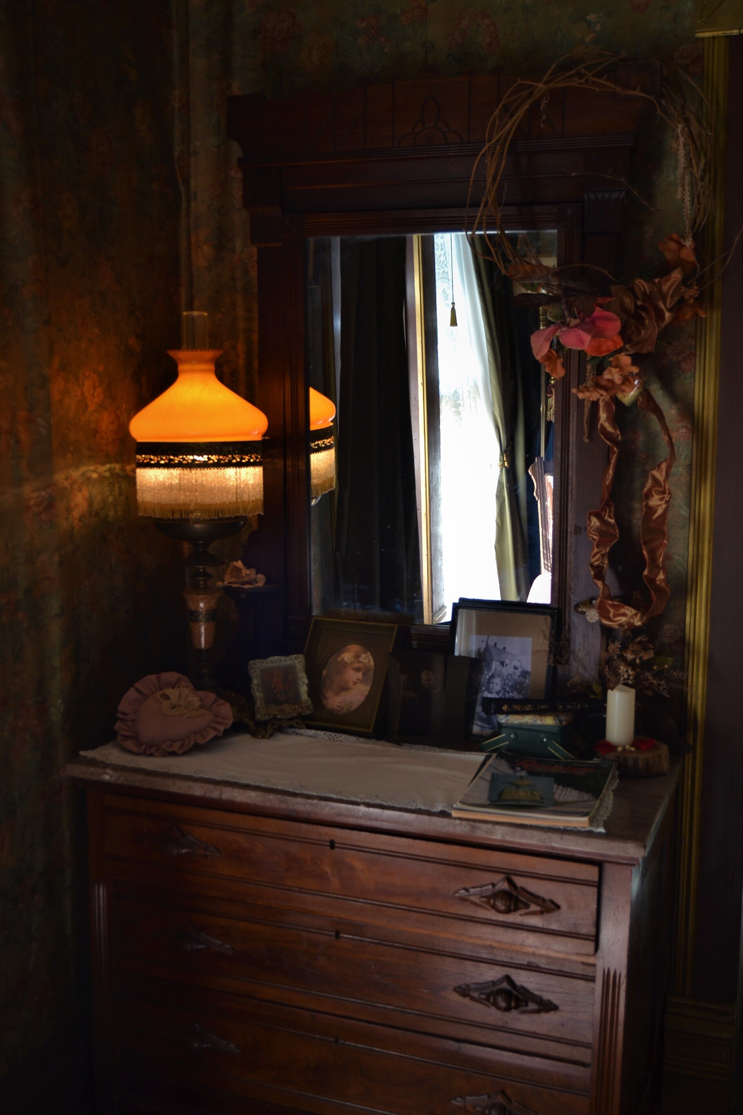 A vintage wooden dresser with a mirror, a lamp, and various personal items.